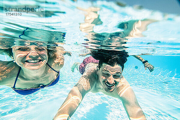 Smiling couple swimming under swimming pool on sunny day