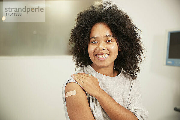 Smiling girl with curly hair showing vaccinated arm in hospital room