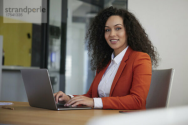 Lächelnde Geschäftsfrau mit Laptop auf dem Schreibtisch am Arbeitsplatz