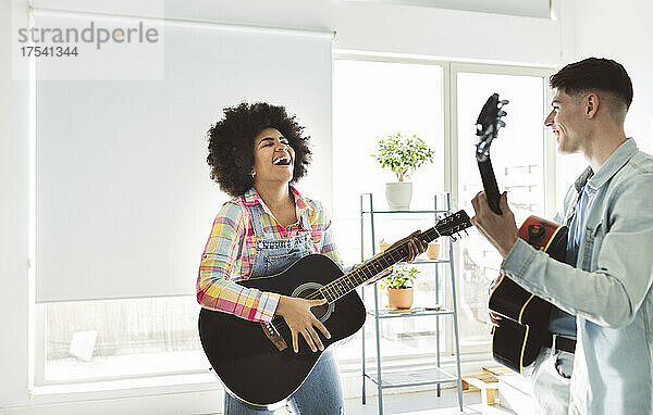 Cheerful young couple playing guitar together at home