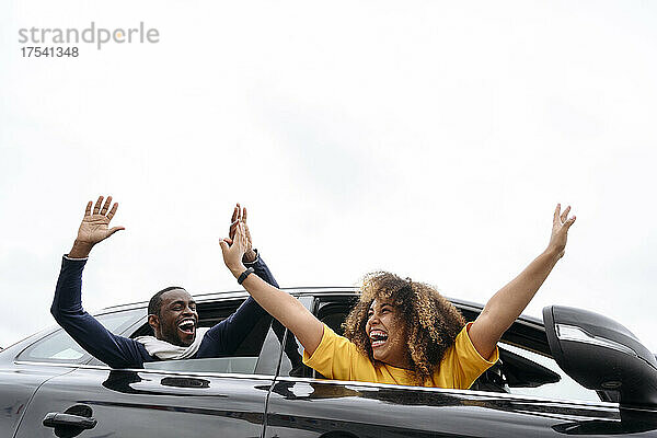 Happy friends leaning out of car windows on road trip