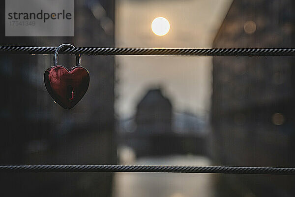 Love lock hanging on bridge railing with setting sun in background