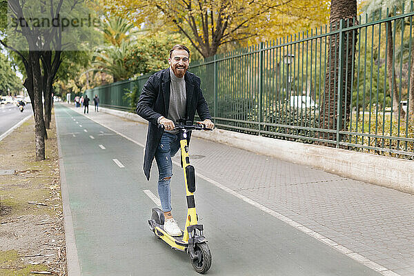 Cheerful man riding e-push scooter on bicycle lane