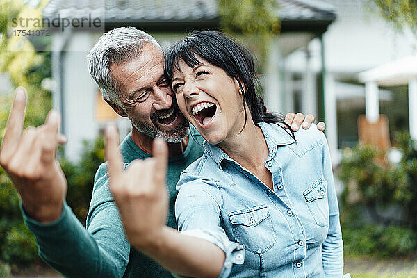 Cheerful making couple gesturing horn sign in backyard