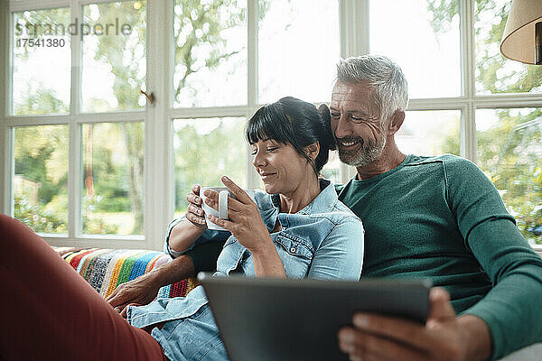 Glücklicher Mann teilt Tablet-PC mit Frau  die zu Hause eine Kaffeetasse hält