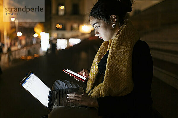 Teenage girl using laptop and smart phone at night