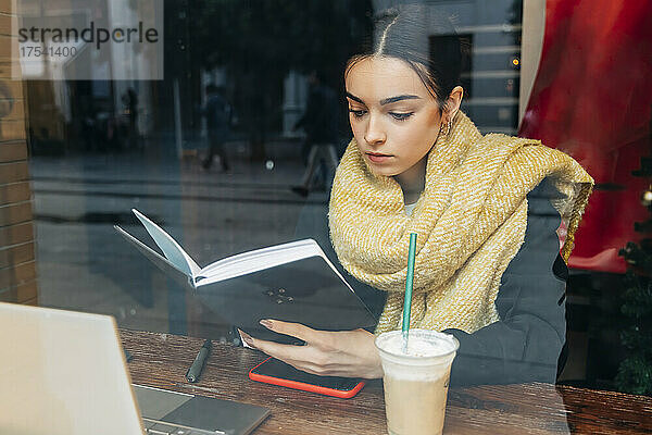 Konzentriertes Mädchen liest Tagebuch am Tisch im Café
