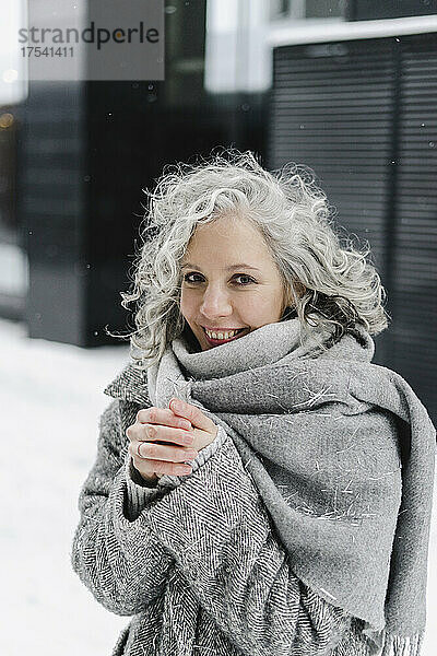 Glückliche Frau wickelte im Winter einen grauen Schal ein