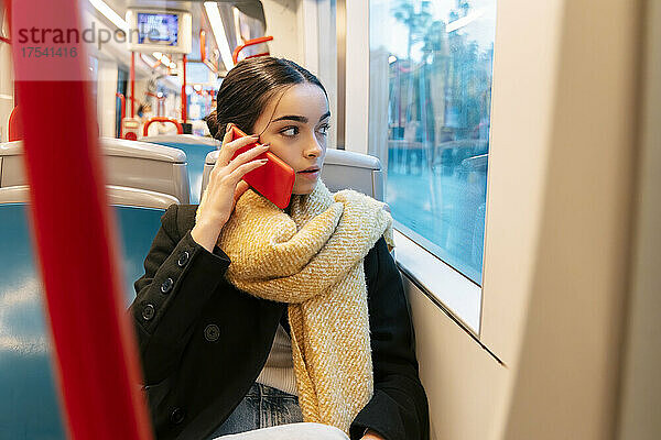 Teenage girl looking through window and talking on smart phone in bus