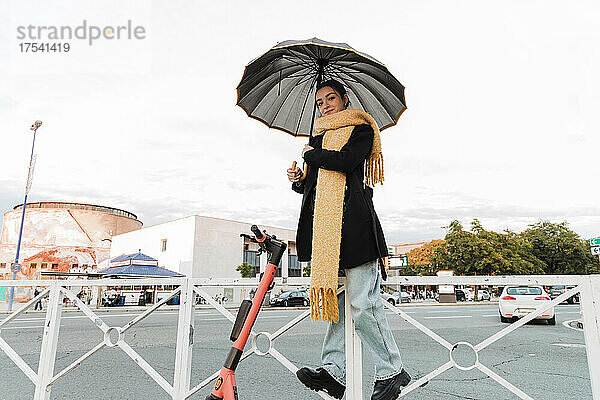 Teenage girl with umbrella standing on railing