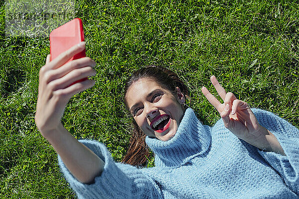 Cheerful woman taking selfie lying down on grass
