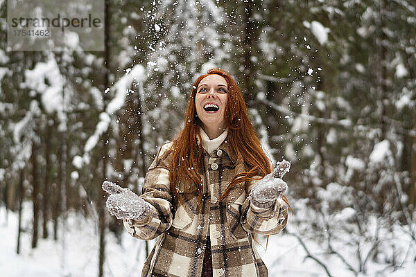 Cheerful woman playing in snow at winter forest