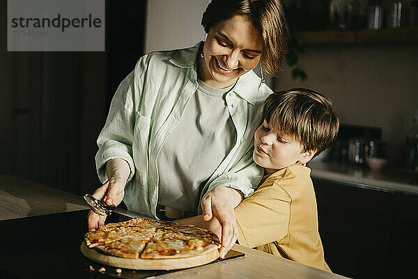 Sohn umarmt Mutter  die zu Hause Pizza und Schneider hält
