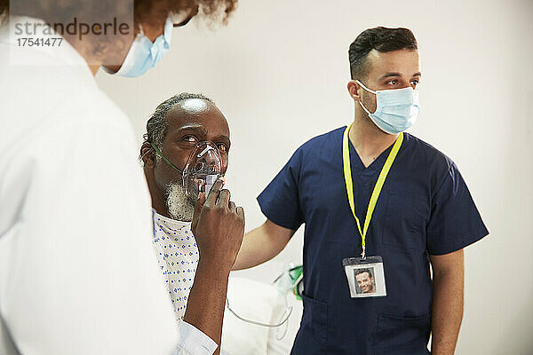 Der Patient passt die Sauerstoffmaske an und blickt den Arzt im Krankenzimmer an