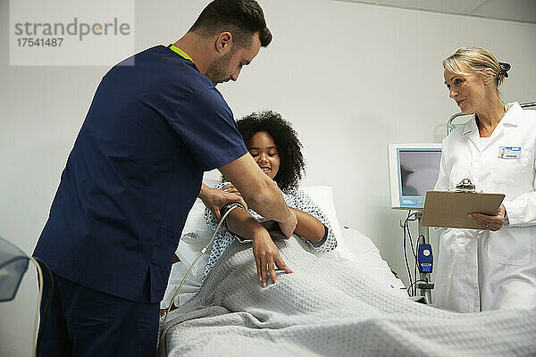 Krankenschwester unterstützt Patient beim Tragen eines Blutdruckmessgeräts auf der Krankenstation