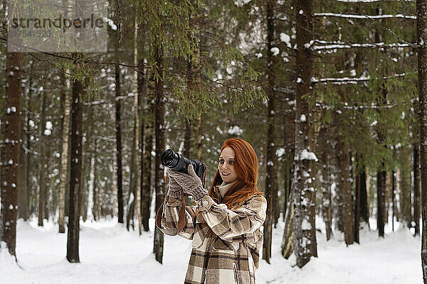 Rothaarige Frau fotografiert mit der Kamera im Winterwald
