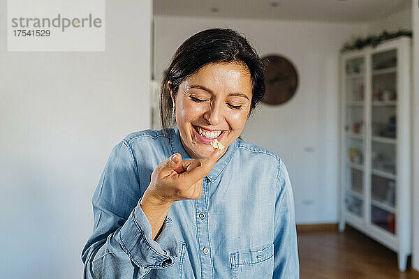 Cheerful woman tasting food with finger at home