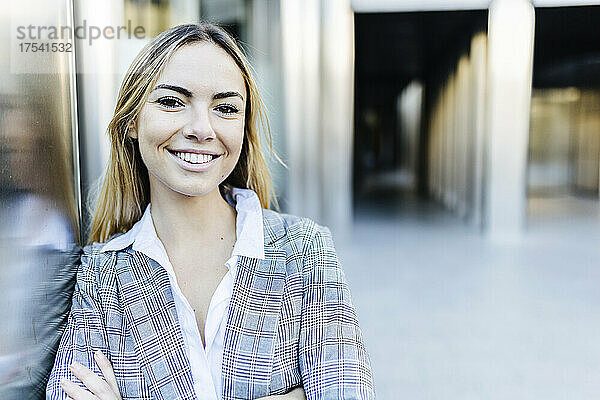 Lächelnde junge blonde Geschäftsfrau lehnt an der Wand