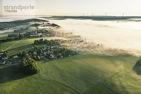 Deutschland  Bayern  Berg  Luftaufnahme eines ländlichen Dorfes im nebligen Frühlingsmorgen