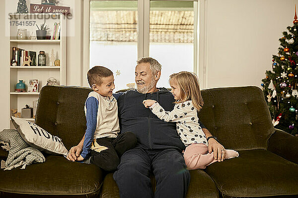 Junge und Mädchen sitzen mit Großvater zu Hause auf dem Sofa