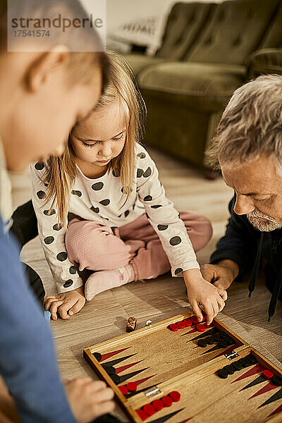 Girl learning backgammon with grandfather at home