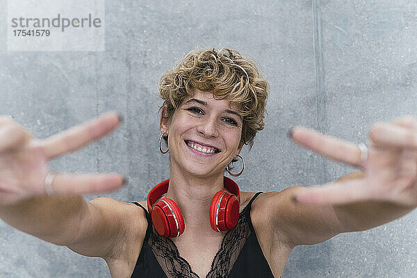 Smiling woman with wireless headphones showing peace sign