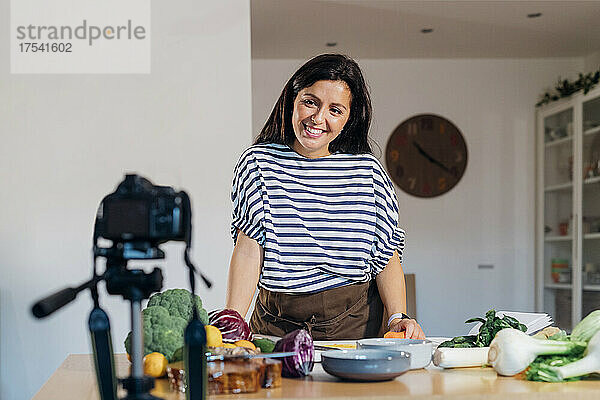 Smiling vlogger making cooking tutorial using camera at home