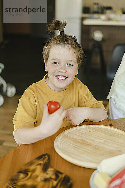 Smiling boy holding tomato at home