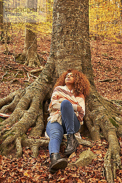 Young woman relaxing by tree in autumn forest