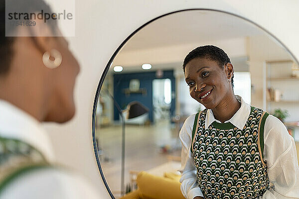 Smiling woman looking at mirror reflection standing in apartment