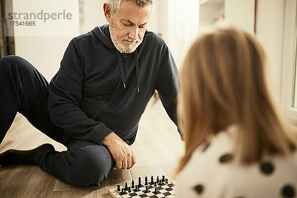 Grandfather playing chess with granddaughter sitting at home