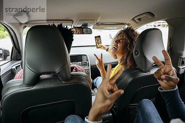 Cheerful woman taking selfie with friends on smart phone in car