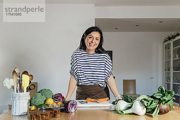 Smiling woman standing at table with fresh vegetables