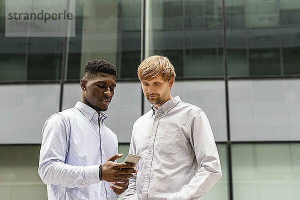 Man sharing mobile phone with friend in front of building
