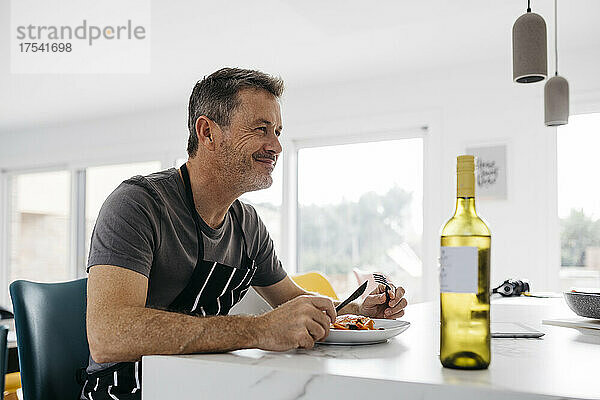 Smiling man holding cutlery eating lunch at home