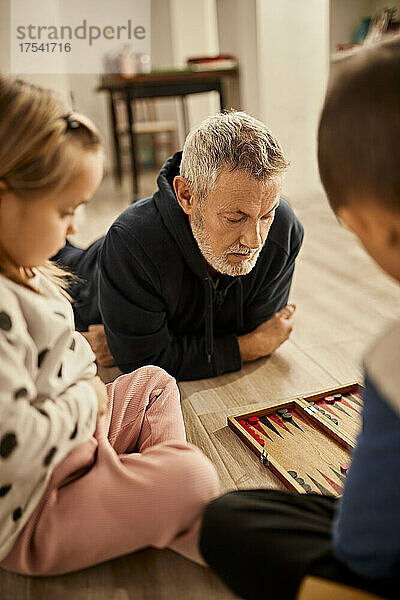 Grandfather lying on floor playing backgammon with grandchildren at home