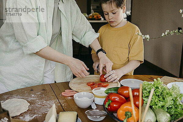 Frau bringt Jungen zu Hause das Schneiden von Tomaten bei