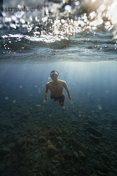 Junger Mann mit Schutzbrille schwimmt unter Wasser