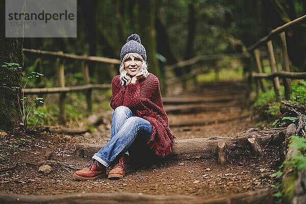 Lächelnde Frau mit den Händen am Kinn sitzt im Wald