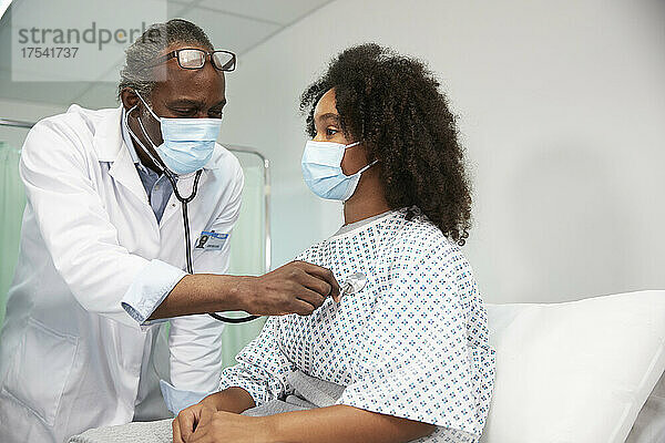 Doctor with protective face mask examining patient in hospital