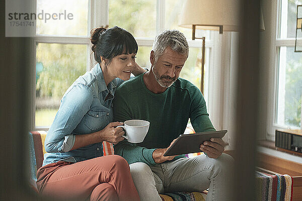 Mann benutzt Tablet-PC und sitzt zu Hause neben Frau mit Kaffeetasse