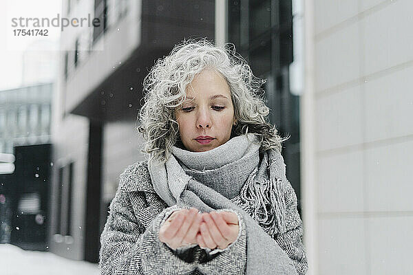 Frau mit grauem Schal schaut im Winter auf die Hände
