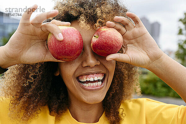 Cheerful woman covering eyes with apples