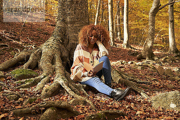 Junge Frau liest Buch am Baum im Herbstwald