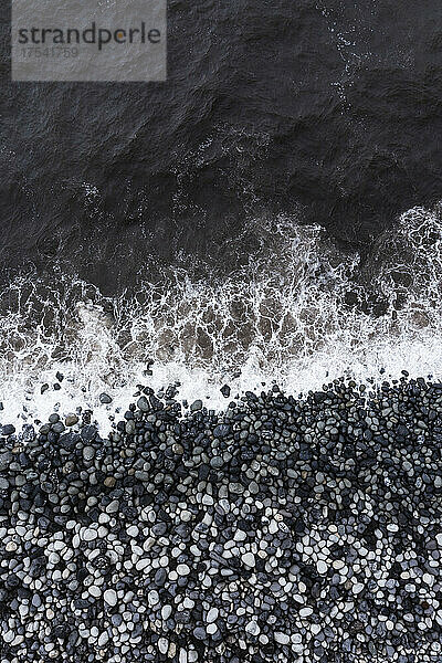 Splashing sea at coastline with pebbles at Rocha da Relva beach
