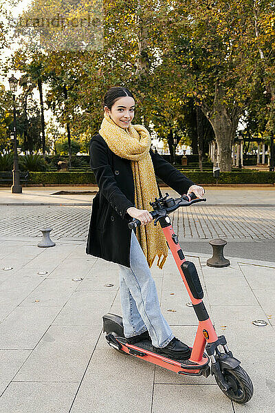 Smiling teenage girl riding electric push scooter on footpath