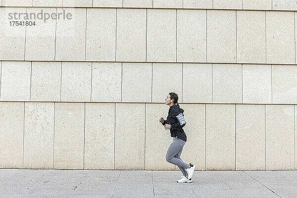 Active woman jogging on footpath by wall