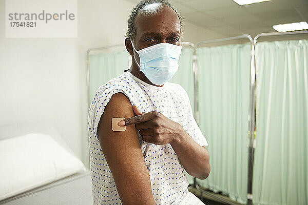 Patient with protective face mask showing vaccinated arm in medical room