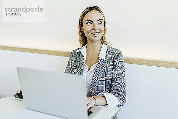 Lächelnde Geschäftsfrau mit Laptop auf dem Tisch im Café