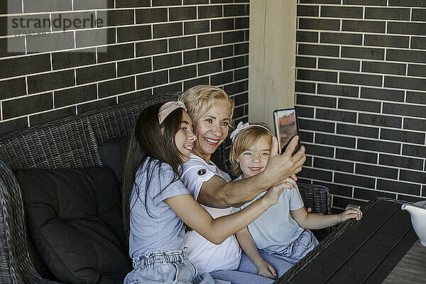 Lächelnde Großmutter macht Selfie mit Enkelinnen auf dem Smartphone